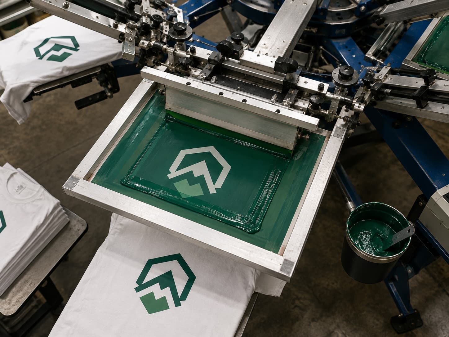 Screen printing press applying a green logo to white t-shirts